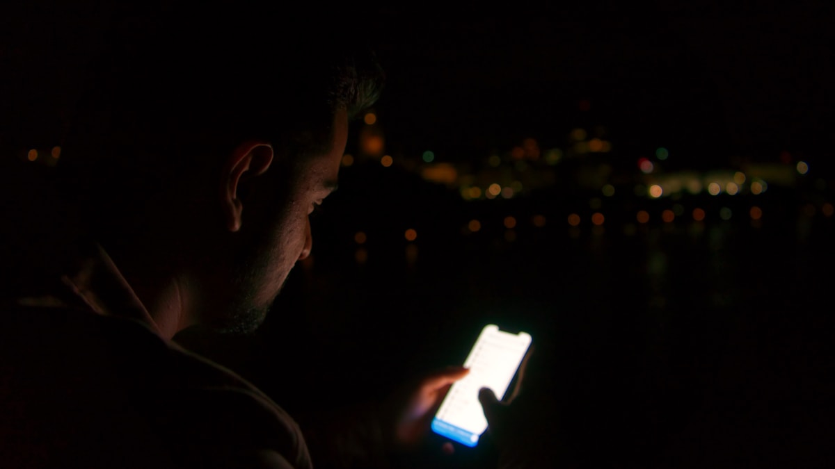 夜にスマートフォンの画面を見つめる人