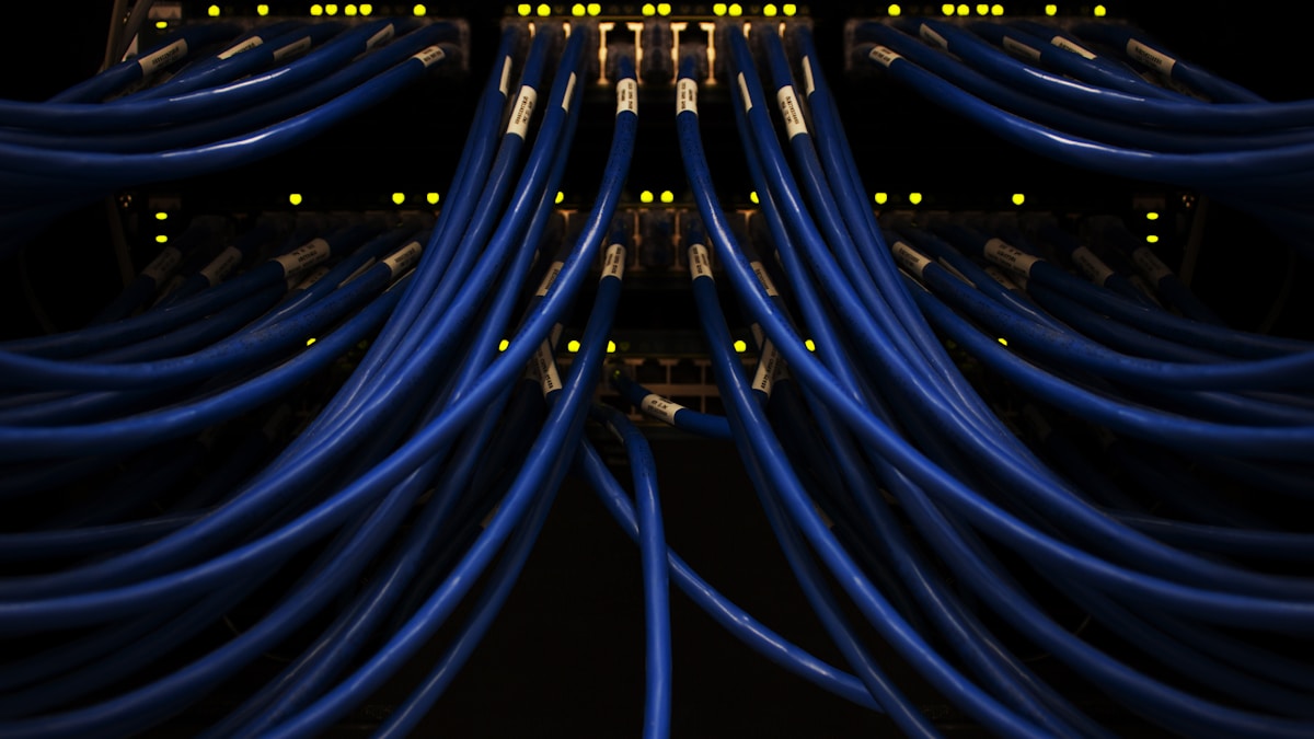 サーバーラックに接続された青いネットワークケーブル群。クラウド上で働くAIエージェントを象徴するイメージ